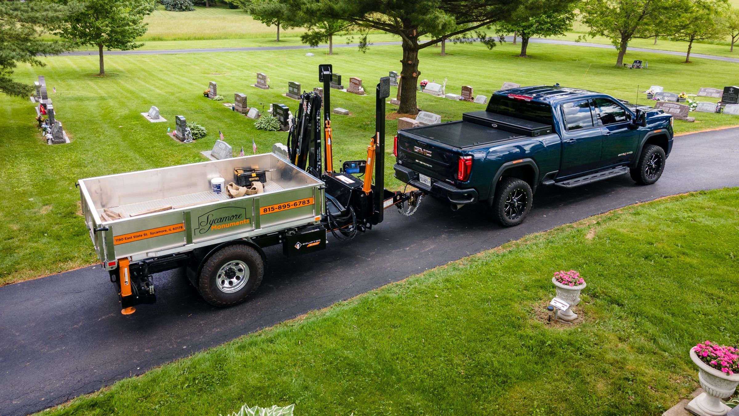 Aerial view of a pickup towing the Equipter 3300 dump trailer along a cemetery lane
